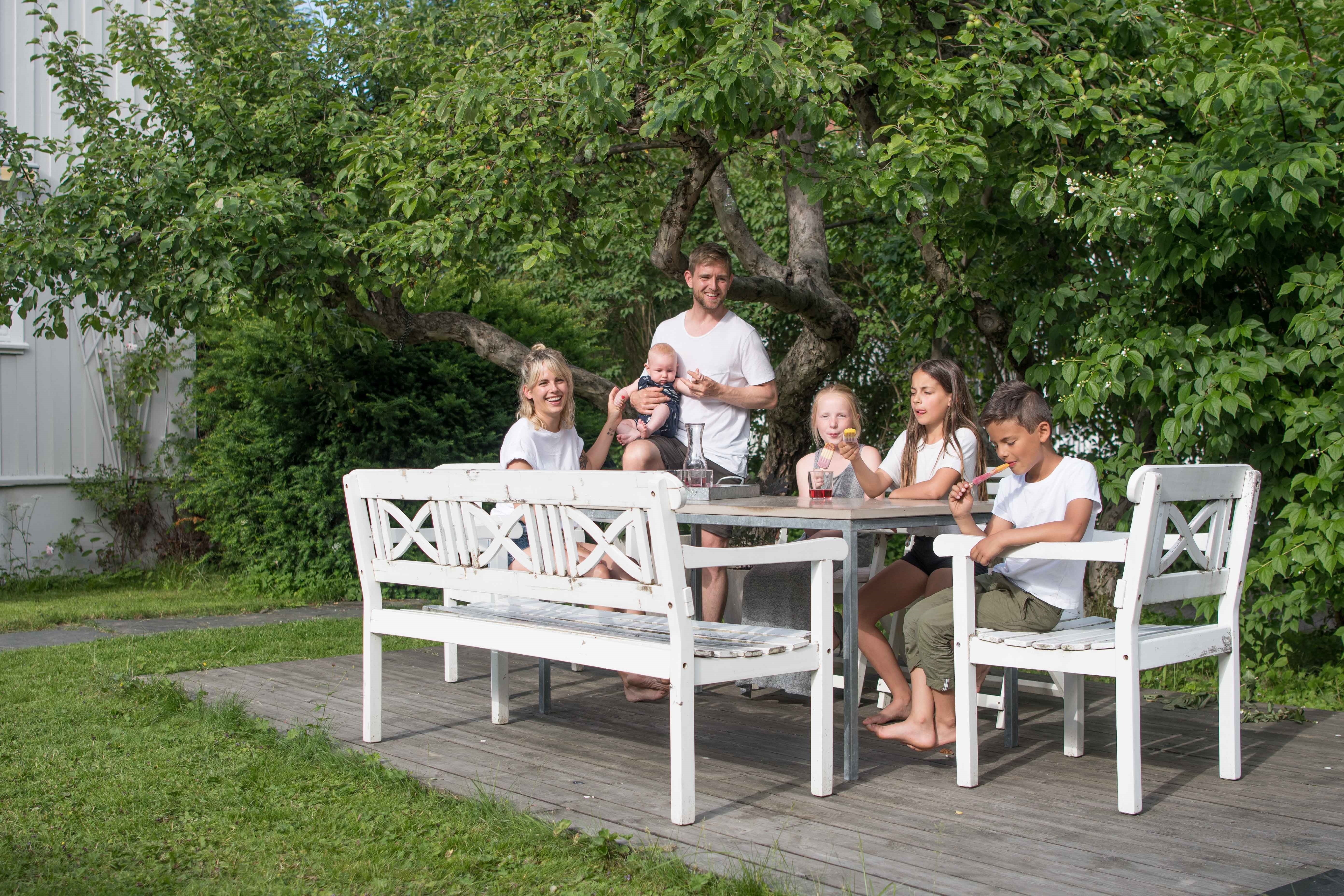 Mor og far og fire barn ved langbord i hagen